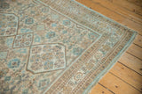 Distressed vintage Hamadan rug corner, featuring pale blue and beige geometric patterns with fringe.