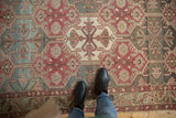 Distressed Baktiari rug featuring muted plum, teal, and ivory geometric and curvilinear panels.