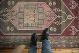 Distressed vintage Malayer rug with geometric blush, aubergine, and charcoal brown patterns.