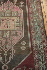 Distressed Malayer rug with blush geometric spandrel against charcoal and aubergine border.