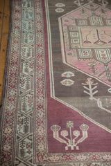 Distressed Malayer rug corner spandrel with geometric patterns in aubergine, charcoal, and blush.