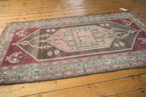 Distressed Malayer rug corner showing faded aubergine, charcoal-brown, and blush geometric patterns.