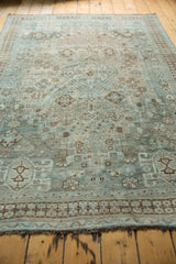 Distressed vintage Shiraz carpet, muted teal, sand, brown tribal patterns with visible wear.