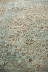 Textured distressed pile of vintage Shiraz carpet showing faded teal and brown tribal motifs.