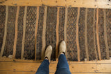 Hand-woven Jijim runner with dark coffee brown and gray geometric bands, showing a worn edge.