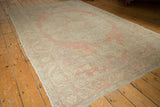 Angled view of distressed Turkish Oushak rug with pale blush, silver, and ivory tones.