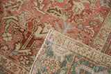 Distressed Heriz rug corner folded, revealing geometric pattern, soft tones, and hand-knotted back.