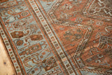 Angled view of distressed Afshar rug, showcasing geometric motifs in rust and pale blue.
