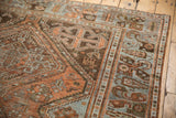Distressed Afshar rug corner, showcasing worn chestnut rust and pale blue geometric patterns.