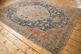 Distressed vintage Sivas carpet corner, featuring worn navy field and blush borders with floral motifs.