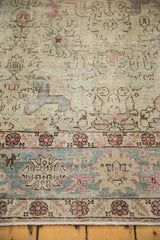 Worn ivory field of a distressed Tabriz carpet with dusty blue and blush pink floral motifs.