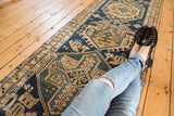 Antique Northwest Persian runner displaying geometric primitive renderings in navy, green, and sand tones, with visible wear.
