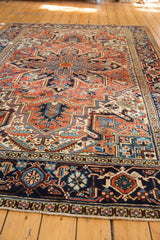 Heriz rug corner: dark navy border, red, blue, ivory geometric patterns, fringe, and even wear.