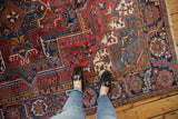 Vintage Heriz carpet with intricate red, blue geometric patterns, floral vinery, and visible fringe.