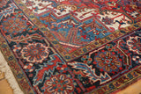 Heriz carpet corner with detailed red, blue, and ivory geometric floral motifs and fringe.