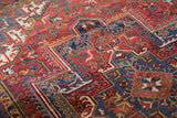 Hand-knotted Heriz carpet, brick red and navy blue, showing scrolling vinery and even wear.