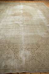 Angled corner view of a distressed vintage Tabriz carpet, showing faded scrolling vinery and worn pile.