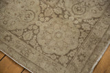 Distressed Tabriz carpet corner, showcasing faded floral motifs in pale coffee brown and ivory.