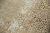 Textured vintage Tabriz carpet close-up, revealing faded ivory vinery and worn foundation.
