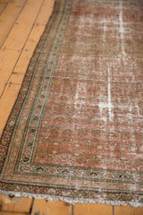 Distressed Malayer rug corner featuring worn blush and sand tones, detailed green border, and fringe.