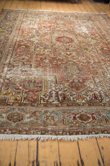 Distressed Heriz rug texture, showing faded terra cotta, slate blue geometric patterns, and fringe.