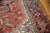 Vintage Heriz carpet: brick red field motifs, ivory and navy blue geometric border detail.