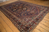 Vintage Shiraz carpet corner with madder root red, navy geometric border, aged pile, and fringe.
