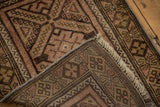 Folded corner of a Belouch rug, showing secured edges, fringe, and geometric pattern in chocolate and blush.