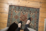 Distressed vintage Afghani mat, geometric tree medallions in ivory, blue, chestnut, with feet.