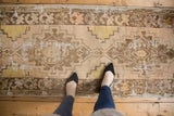 Distressed Oushak runner with worn geometric patterns in soft beige, sand, and coffee.