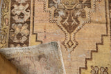 Curled corner of vintage Oushak runner, showing distressed saffron pile and hand-knotted foundation.