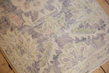 Distressed pile of vintage Oushak rug with faded violet, green, and ivory floral elements.