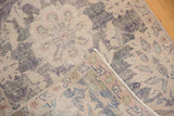 Distressed Oushak rug corner revealing hand-knotted foundation with blue, pink, and green threads.