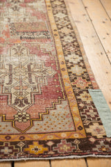 Distressed Oushak runner: worn geometric patterns, chocolate brown border, and green patchwork.