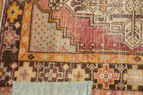 Distressed Oushak rug corner with geometric dusty aubergine, saffron yellow, and pale green sewn patch.