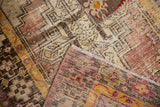 Distressed patchwork Oushak runner with layered textures and wear in aubergine and saffron.