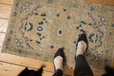 Worn Hamadan rug close-up, distressed texture with floral patterns in beige, mint, navy.