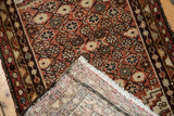 Folded corner of distressed Hamadan rug showing hand-knotted foundation, fringe, and pile wear.
