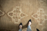Distressed vintage Oushak carpet with worn low pile, soft sand and coffee brown medallion patterns.