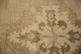 Distressed Oushak carpet detail showcasing faded beige and coffee brown curvilinear motifs.