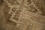 Close-up of distressed Oushak rug, showing low pile, hand-knotted back, and beige sand tones.