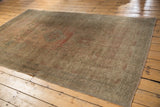 Corner of distressed Oushak carpet with worn texture, low pile, and muted rose-green tones.