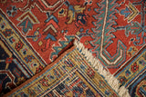 Vintage Heriz carpet's folded corner reveals hand knotted back, cherry red geometric pattern, cream fringe.