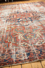 Distressed pile of vintage Heriz rug, with brick red, navy, sky blue geometric motifs.
