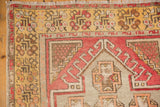 Fringed corner of a distressed Oushak runner, showing saffron yellow border and blush geometric patterns.