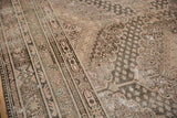 Distressed Khotan carpet's worn pile, revealing geometric borders, scalloped contours in pale rose and oxidized shades.