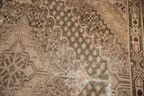 Distressed Khotan carpet texture with visible foundation wear, beige and time-softened brown tones.