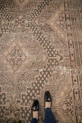 Feet on vintage distressed Khotan carpet, showing faded rose, oxidized silver geometric patterns.