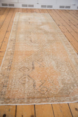 Vintage Distressed Oushak runner's worn pile, revealing faded apricot, ivory, and scrolling rams horn motif.