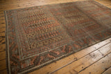 Angled view of a vintage Belouch rug with repeating tree of life panels in earthy tones.